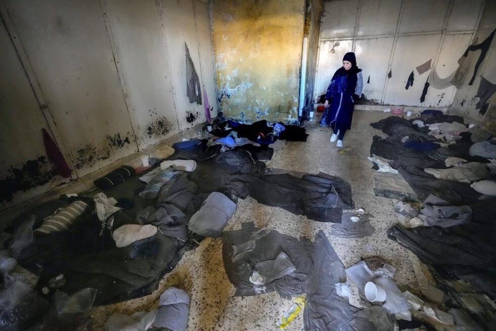 Una mujer observa mantas y otras prendas de ropa tiradas en el suelo de una habitación de la prisión militar de Saydnaya, al norte de Damasco, Siria, el lunes 9 de diciembre de 2024.