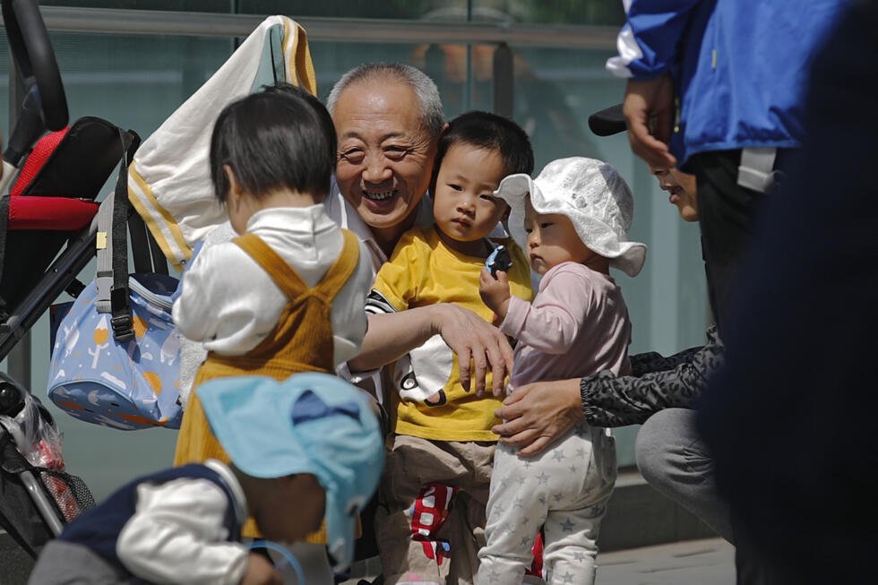 An elderly man plays with children near a commercial office building in Beijing on May 10, 2021. China's ruling Communist Party will ease birth limits to allow all couples to have three children inst