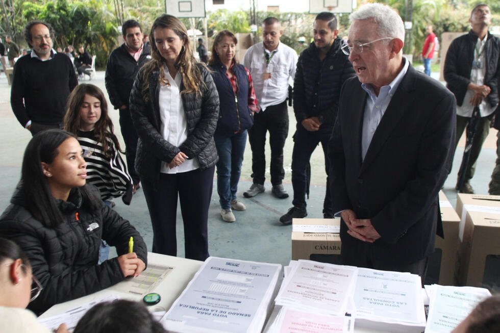 El expresidente colombiano Álvaro Uribe, a la derecha, habla con un funcionario electoral antes de votar durante las elecciones legislativas en Rionegro, Colombia, el domingo 8 de marzo de 2026.