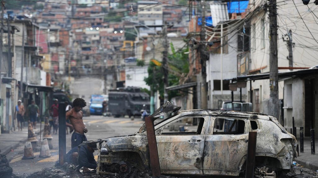 Varias personas retiran piezas útiles de un coche incendiado que había sido utilizado como barricada por presuntos narcotraficantes durante una operación policial en la favela Complexo do Alemão, donde opera la organización criminal 'Comando Vermelho' en Río de Janeiro, el martes 28 de octubre de 2025.